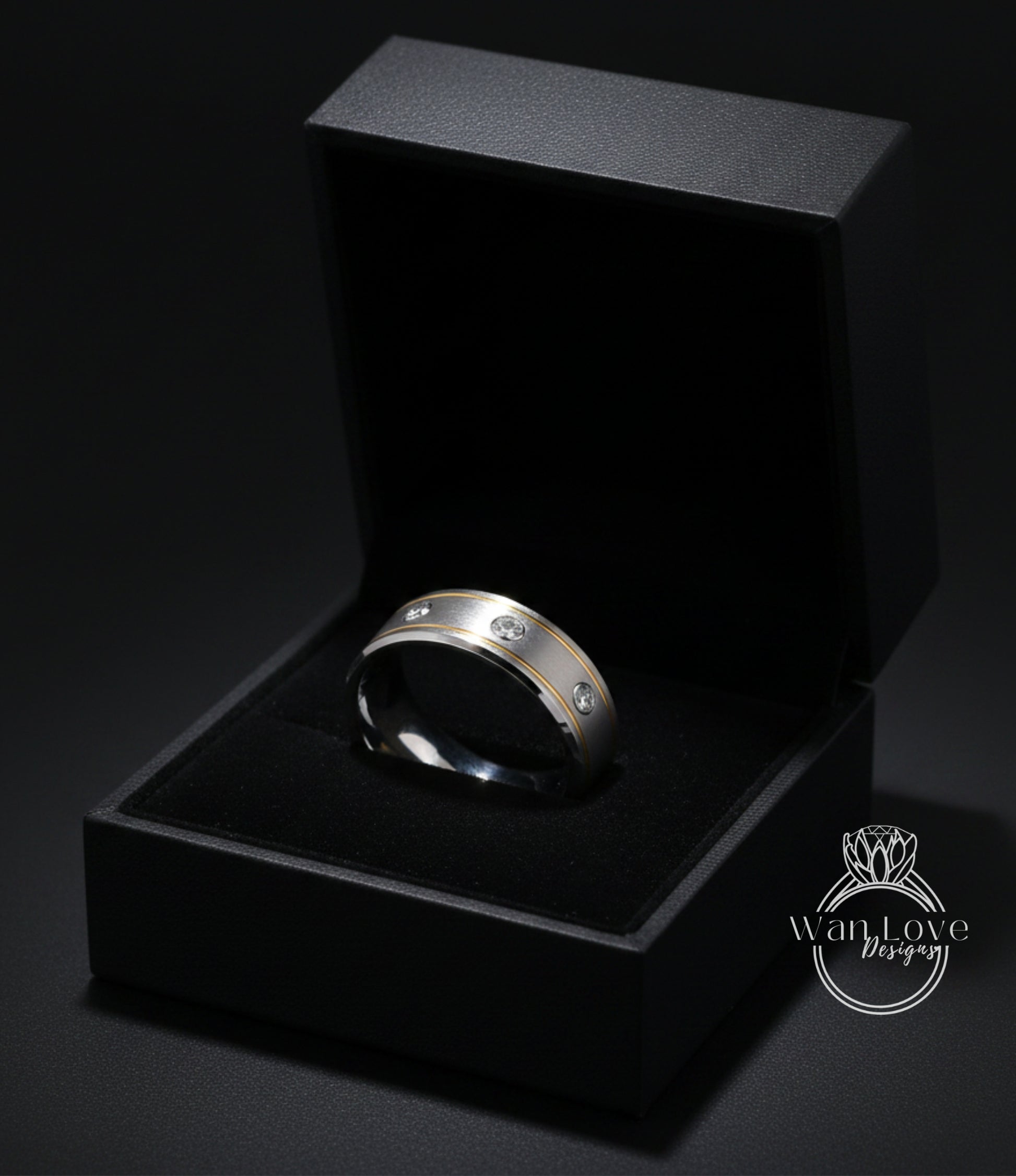 A silver ring with three diamonds is displayed in a black jewelry box against a dark background.
