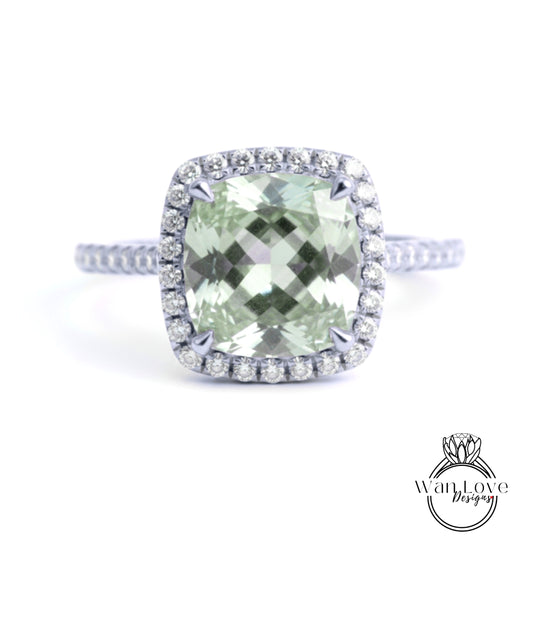 A diamond ring with a large, square-cut green gemstone surrounded by a halo of smaller diamonds set in a silver band.