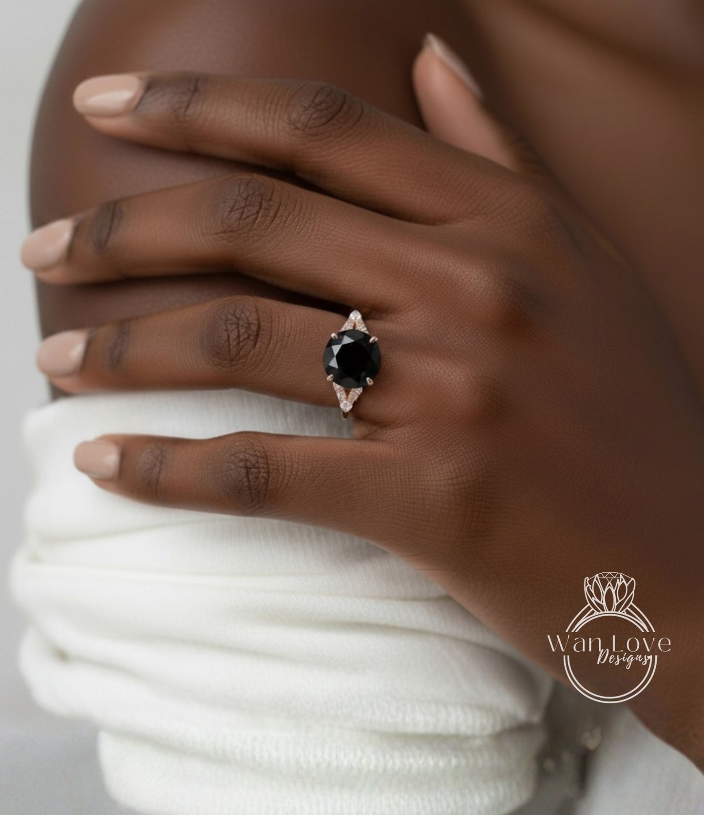 A close-up of a hand wearing a ring with a large black gemstone, resting on a white fabric.