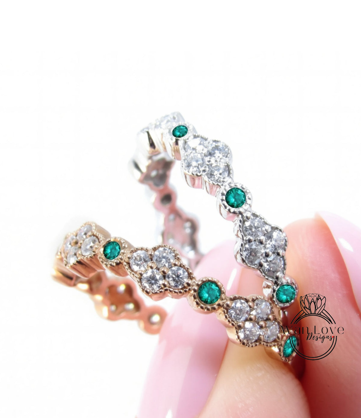 A close-up of a person's hand holding a ring with a combination of gold and silver elements, including diamonds and green gemstones.