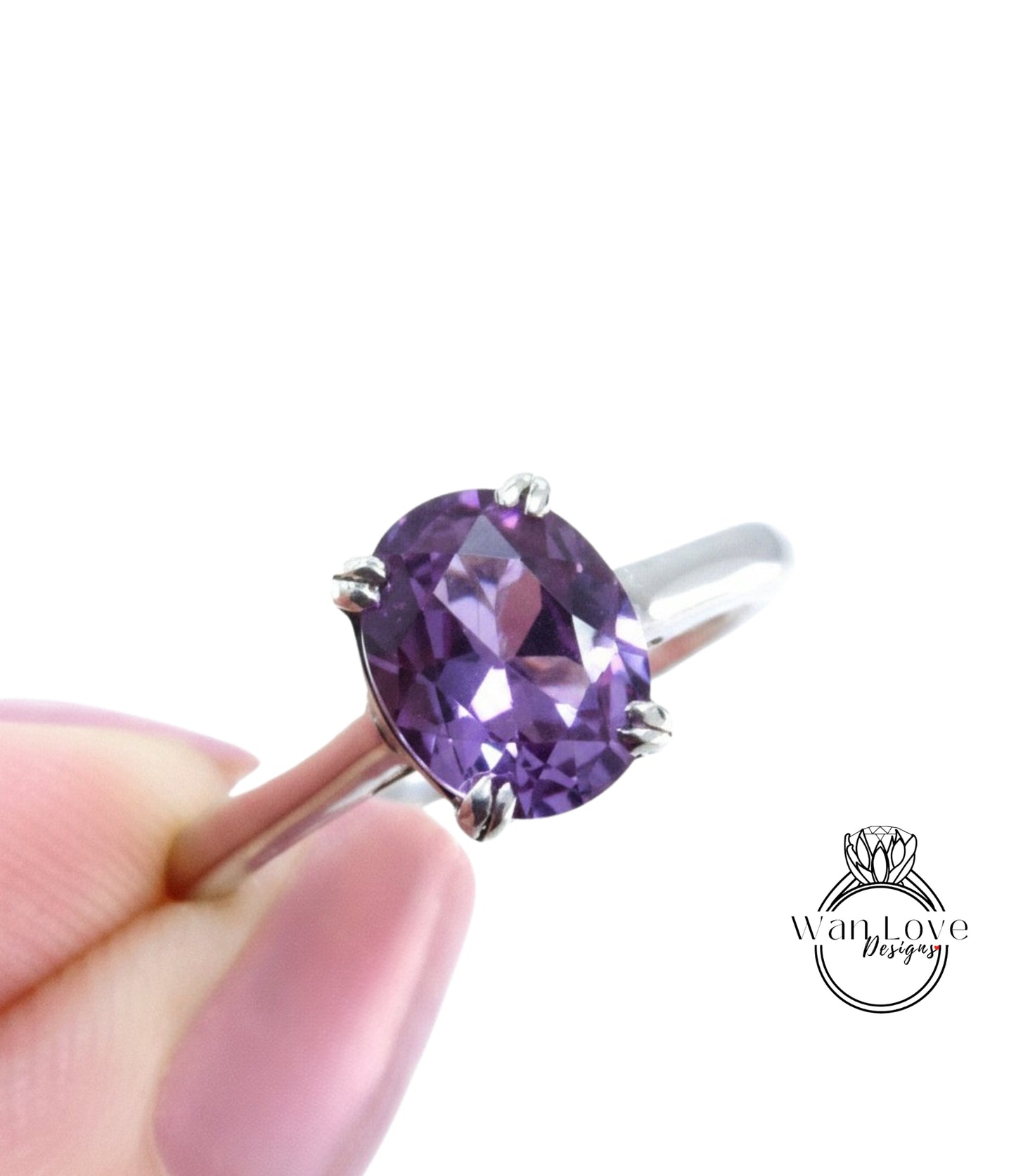 A close-up image of a person's hand holding a silver ring with a large, oval-shaped purple gemstone.