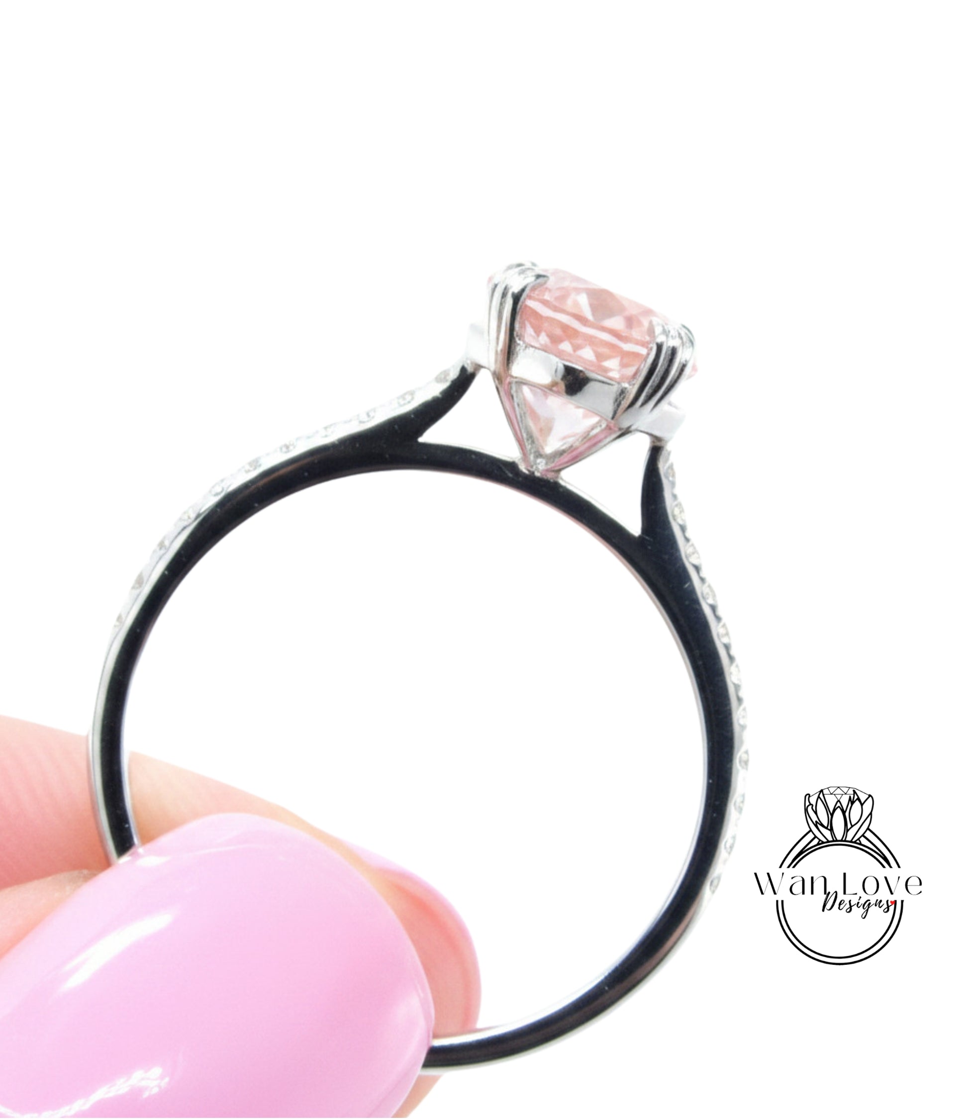 A close-up of a person's hand holding a silver ring with a pink gemstone, against a white background.