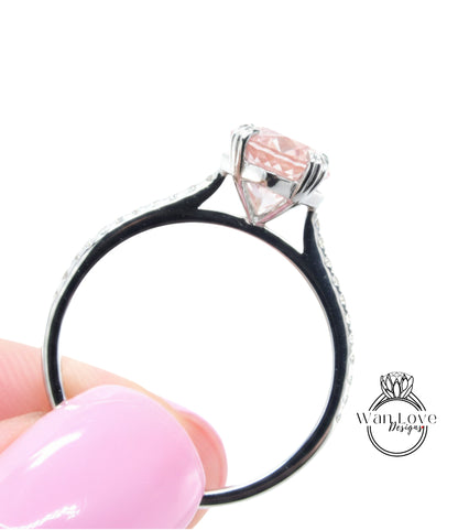 A close-up of a person's hand holding a silver ring with a pink gemstone, against a white background.