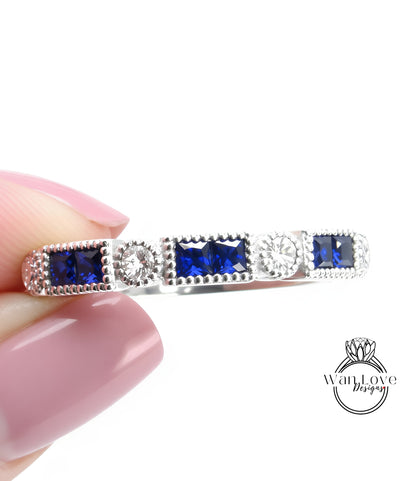 A close-up image of a person's hand holding a silver ring adorned with blue gemstones.