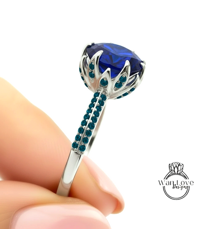 A close-up image of a person's hand holding a silver ring with a large blue gemstone, likely a diamond, and small blue gemstones around it.