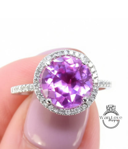 A close-up image of a person's hand holding a ring with a large, round purple gemstone surrounded by a halo of smaller diamonds.