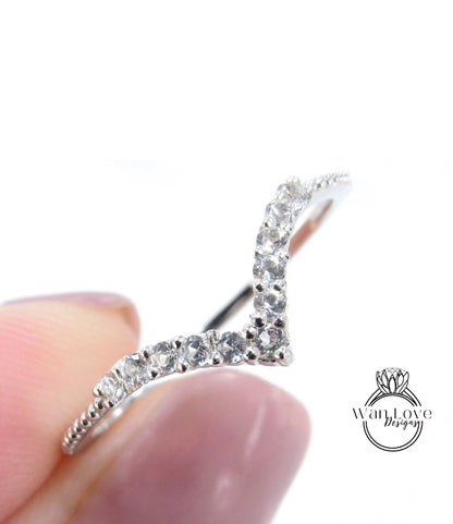 A close-up image of a silver ring with a v-shaped design and small diamonds set in it, held in someone's hand.