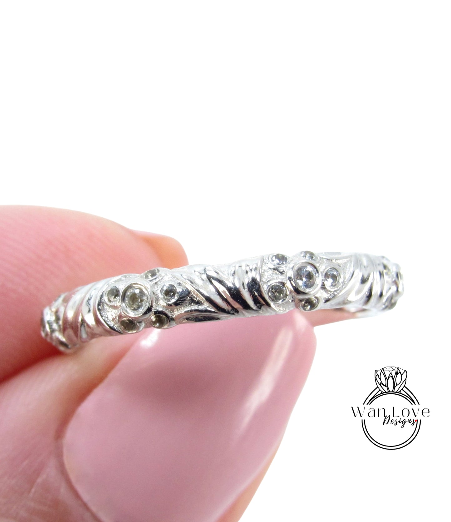 A close-up image of a person's hand holding a silver ring with a floral design.