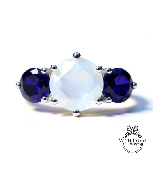 A silver ring with a large white gemstone and two blue gemstones.