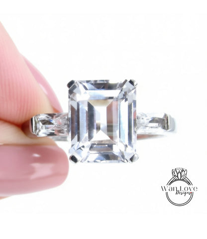 A close-up of a person's hand holding a diamond engagement ring with a large, clear gemstone.