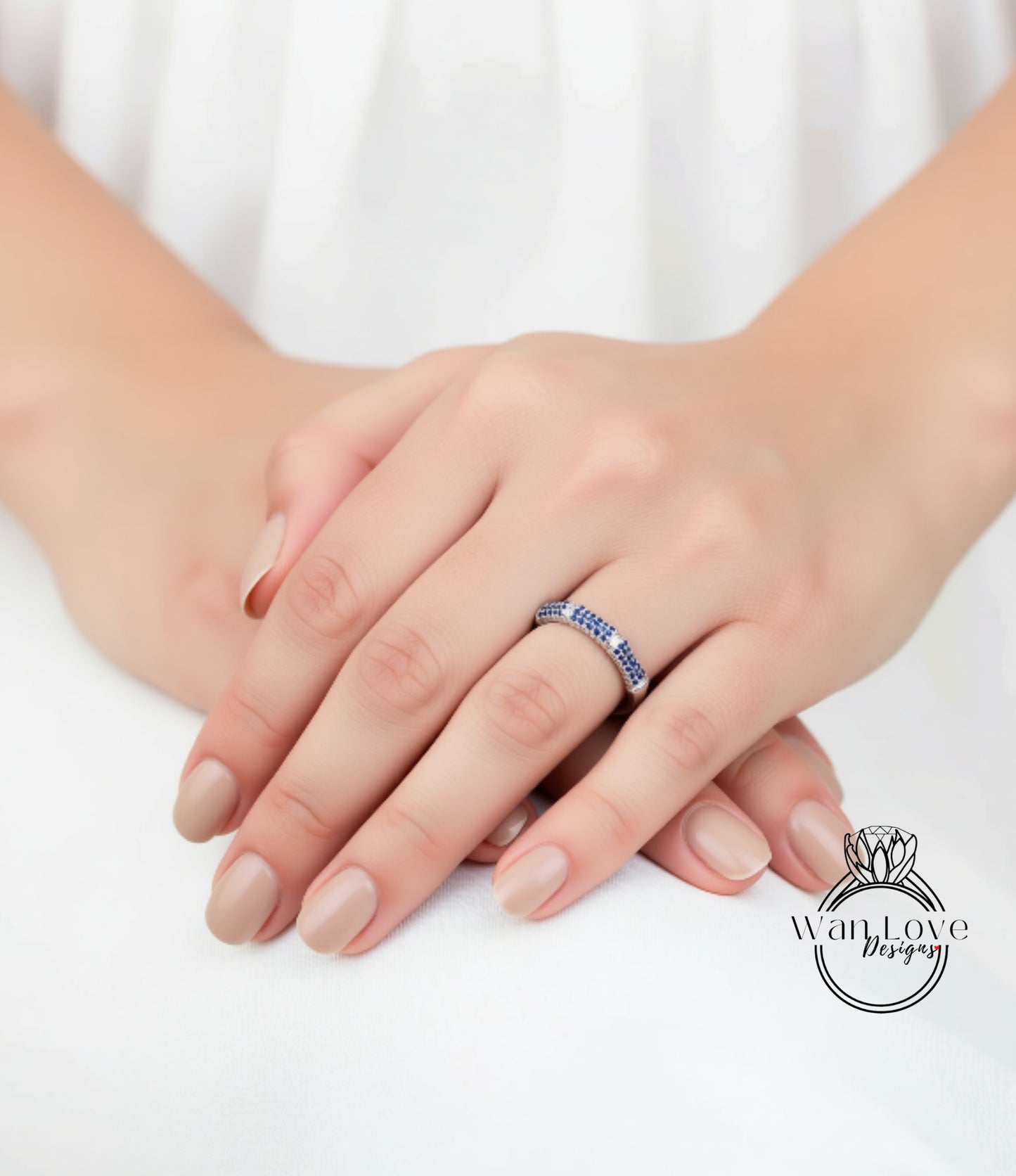 A close-up image of a person's hands wearing a ring with blue stones.