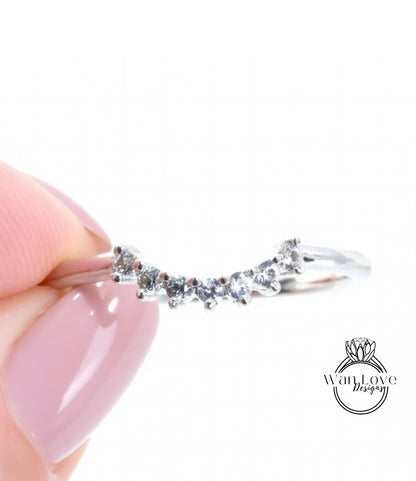 A close-up of a person's hand holding a silver ring with a row of small diamonds on it.