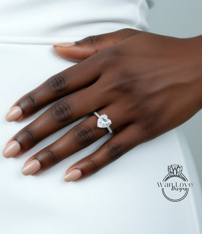 A close-up of a hand wearing a diamond engagement ring with a heart-shaped diamond.