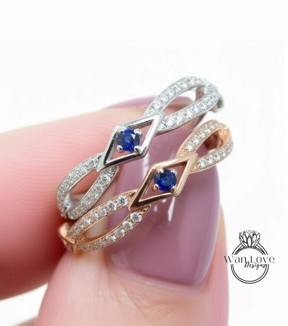 A close-up of a person's hand wearing a ring with two diamond-encrusted designs, one with a blue gemstone and the other with a gold gemstone.