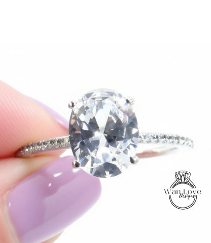 A close-up of a person's hand holding a diamond engagement ring with a large oval-shaped diamond set in a silver band.