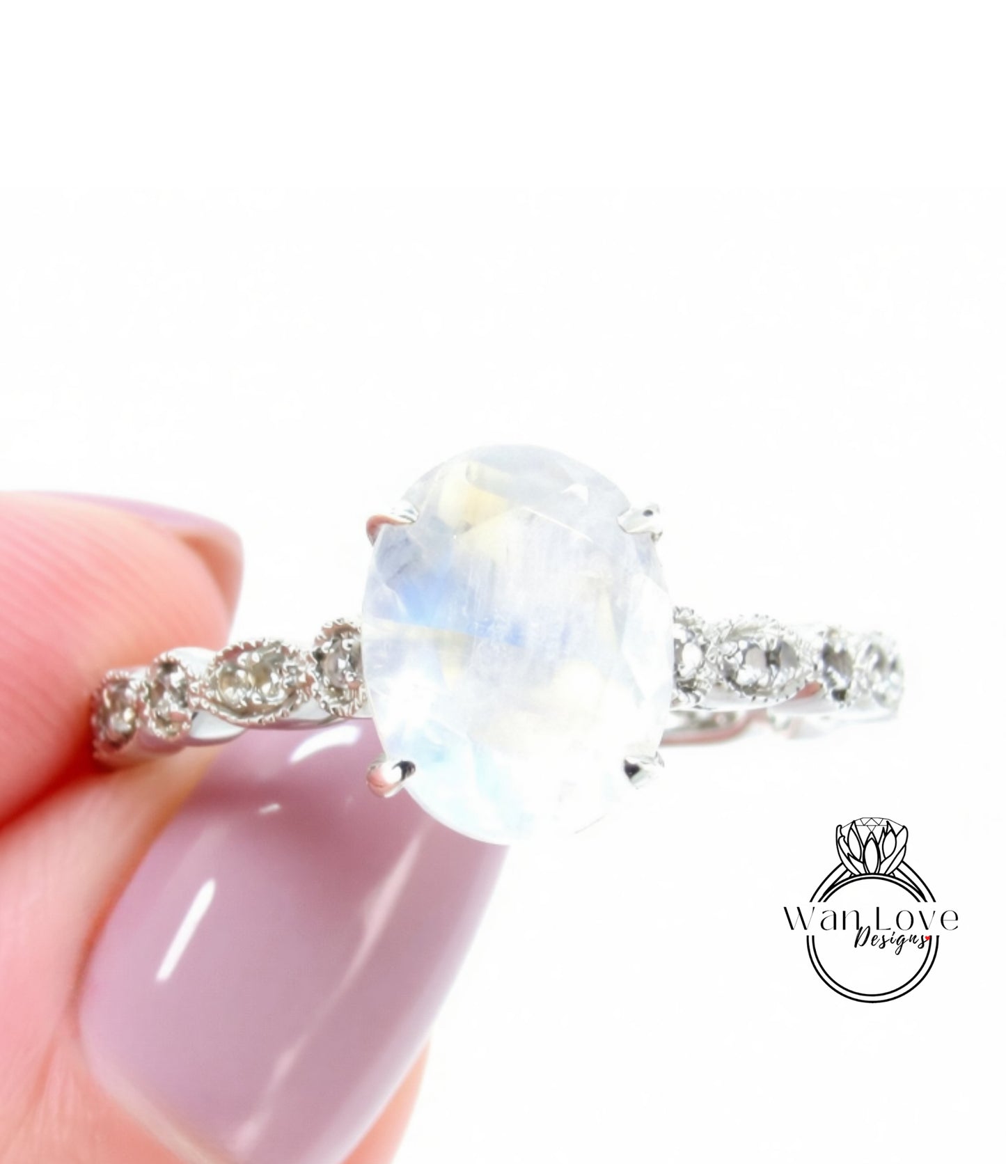 A close-up of a person's hand holding a ring with a large oval-shaped gemstone, likely a moonstone, set in a silver band.