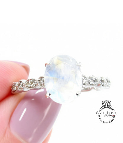 A close-up of a person's hand holding a ring with a large oval-shaped gemstone, likely a moonstone, set in a silver band.