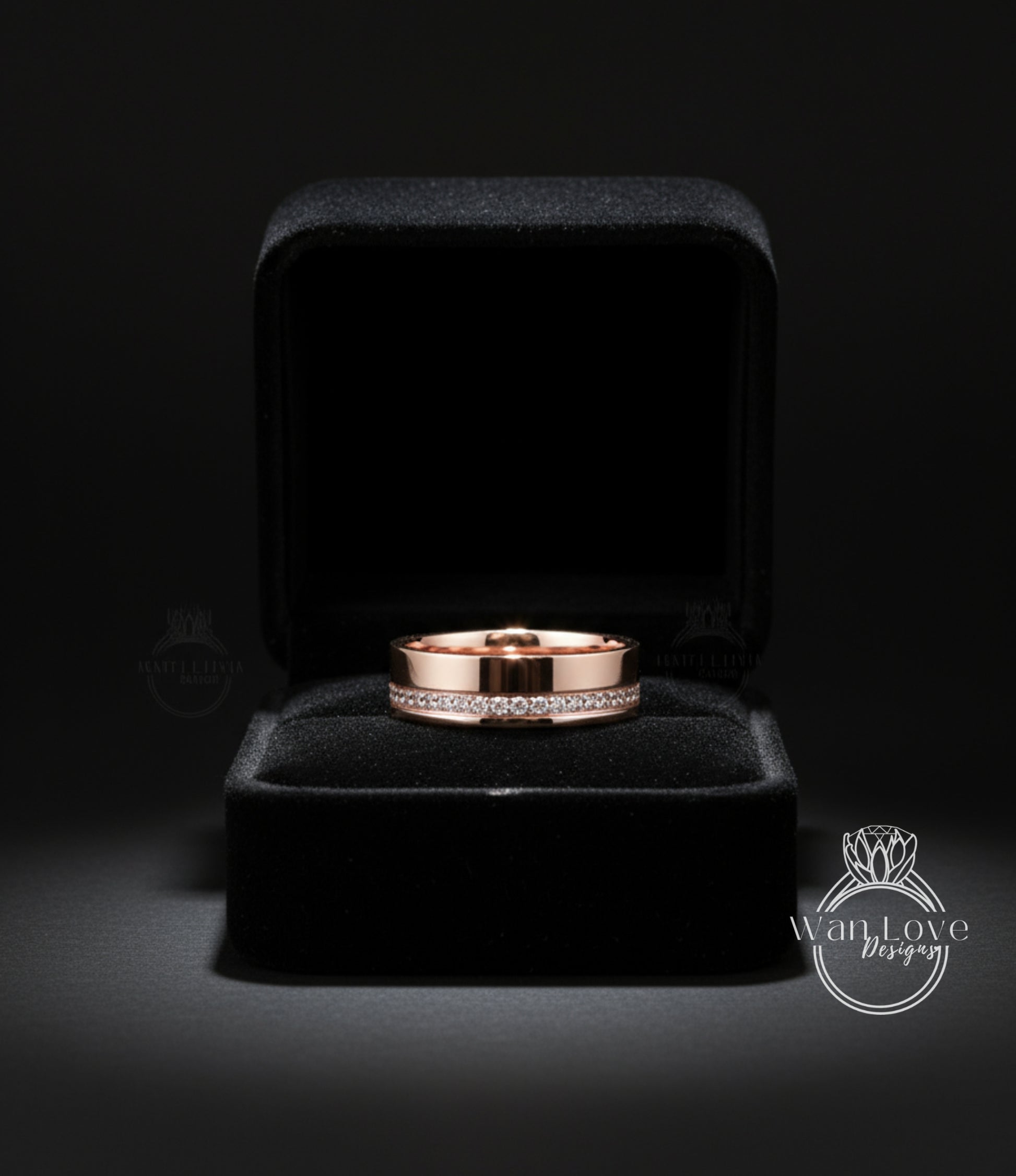 A gold wedding band with a diamond band is displayed in a black velvet jewelry box against a dark background.