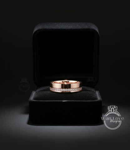 A gold wedding band with a diamond band is displayed in a black velvet jewelry box against a dark background.