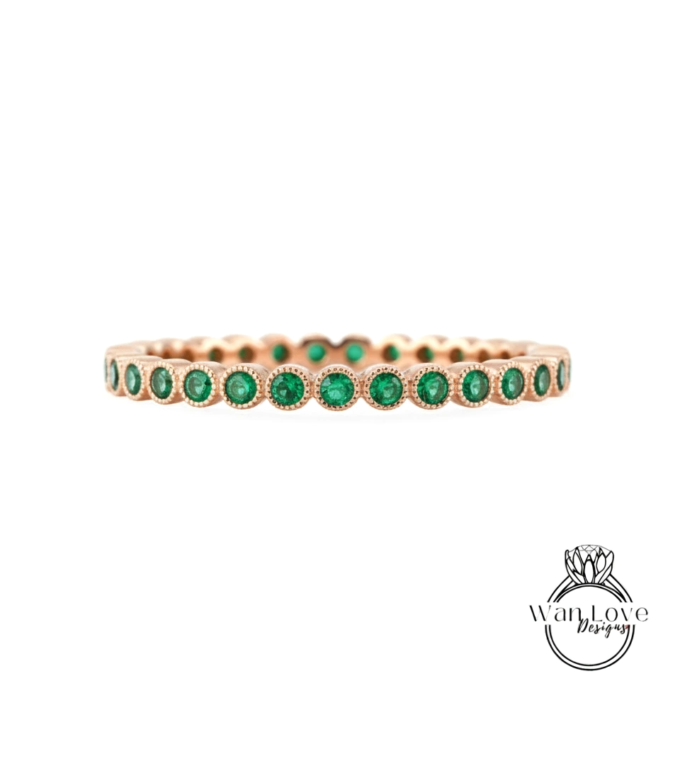 A gold-colored ring with a row of green gemstones, likely emeralds, set in the center.