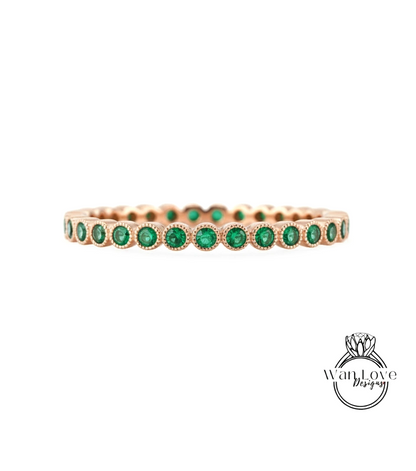 A gold-colored ring with a row of green gemstones, likely emeralds, set in the center.