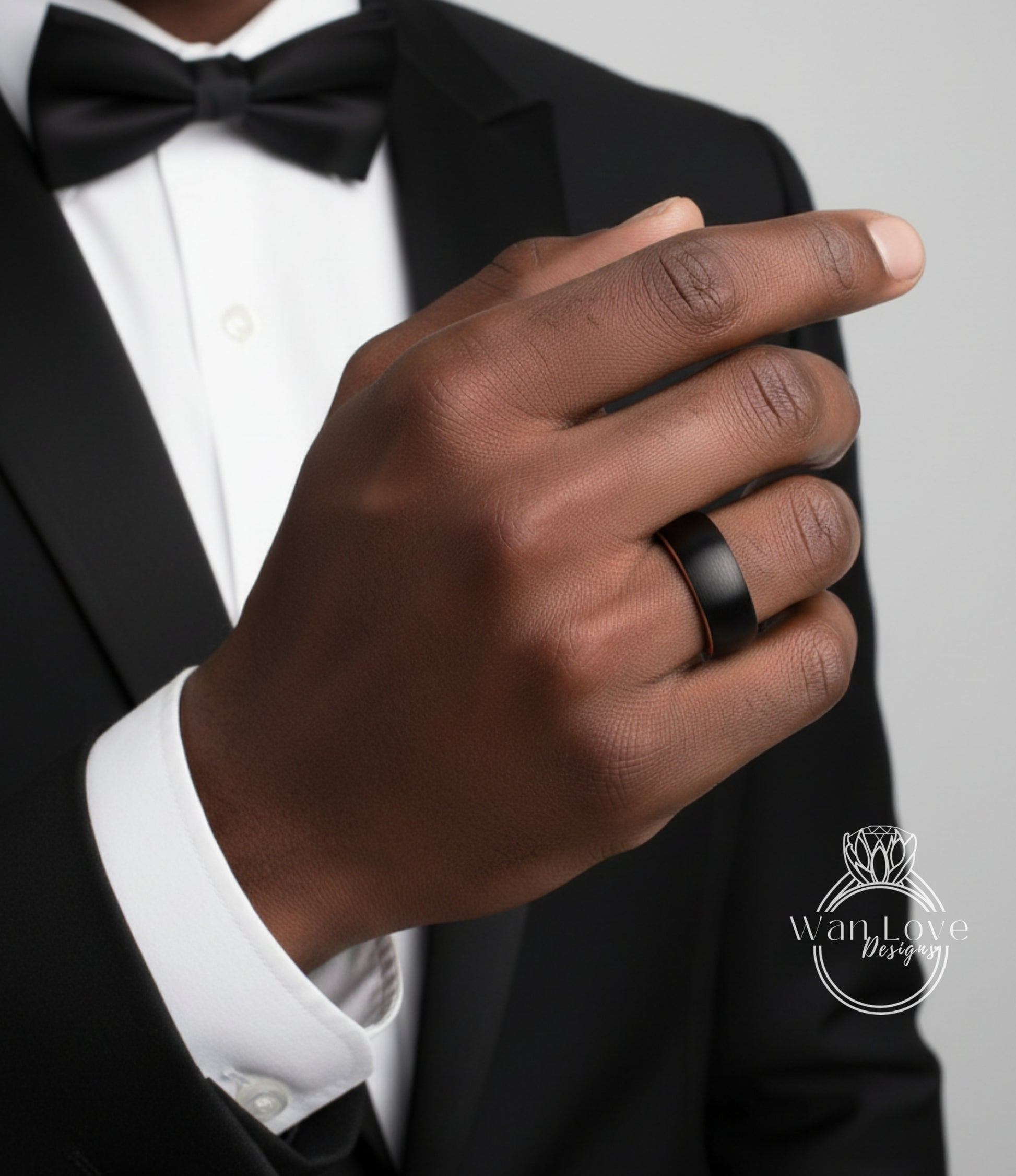 A close-up of a person's hand wearing a black ring, with a black bow tie and a white shirt underneath.
