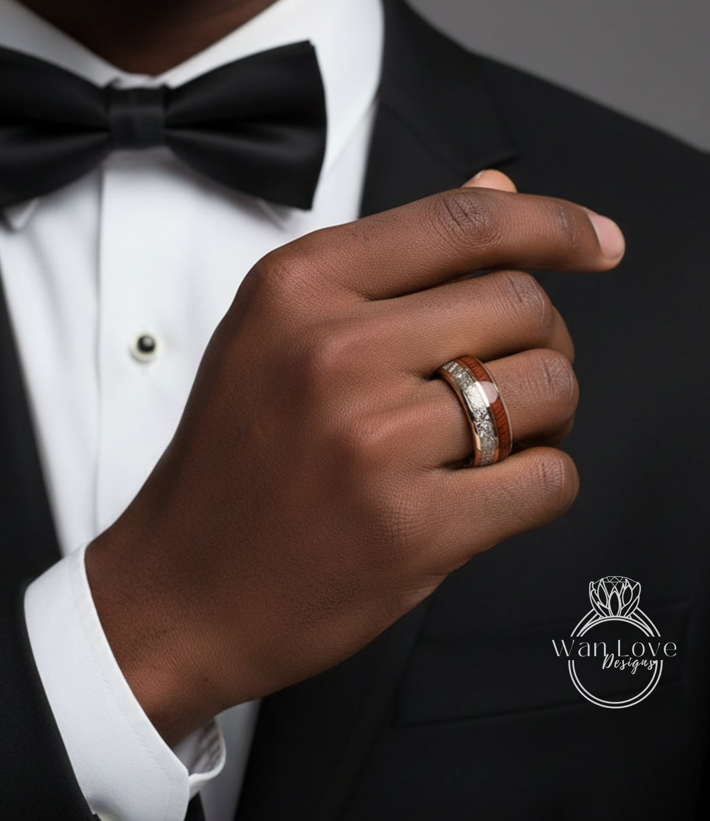 A close-up of a person's hand wearing a black bow tie and a ring on their finger, with a black suit jacket visible.