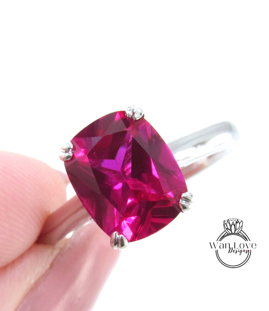 A close-up image of a person's hand holding a ring with a large, bright pink gemstone.