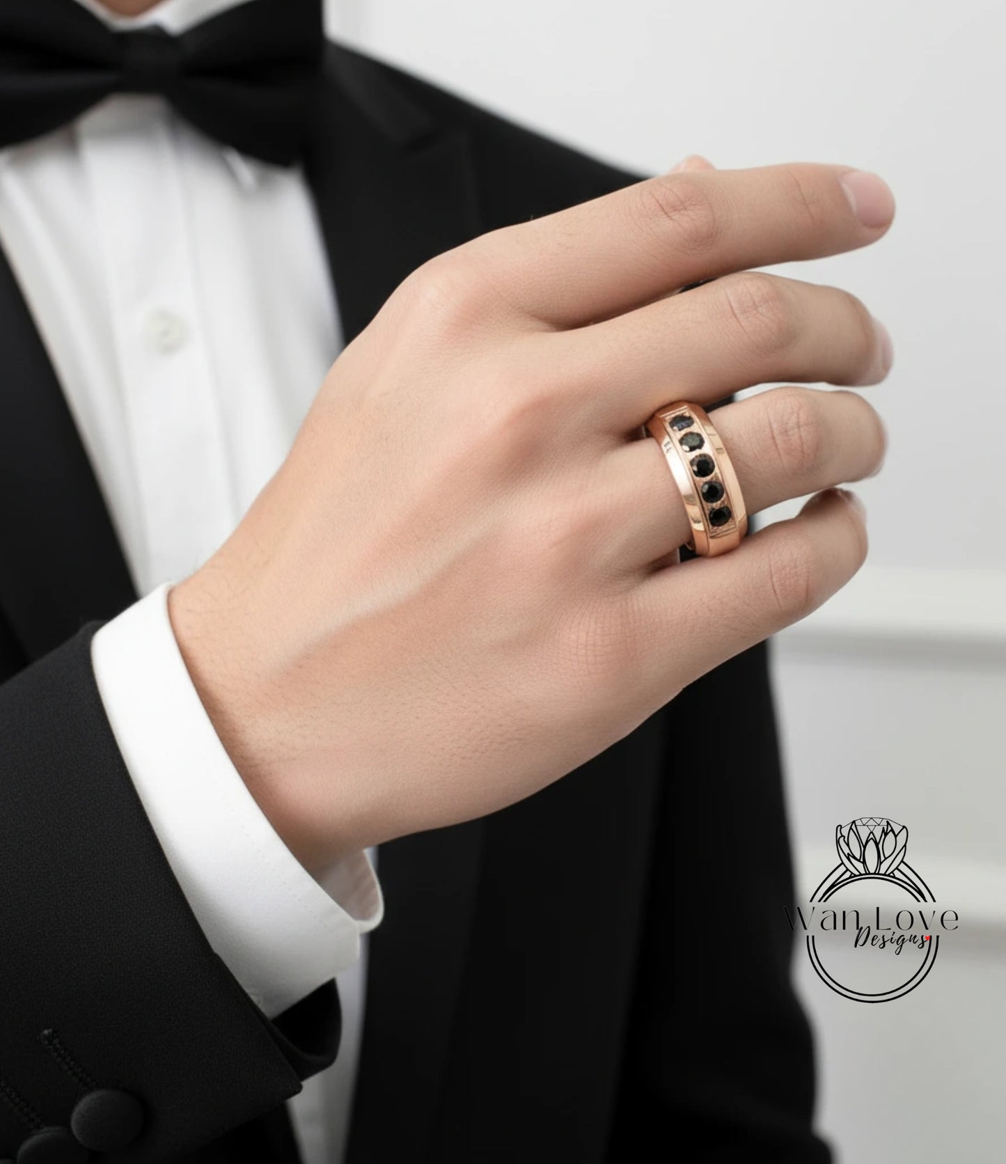 A close-up of a person's hand wearing a gold ring with black stones, wearing a black tuxedo jacket.