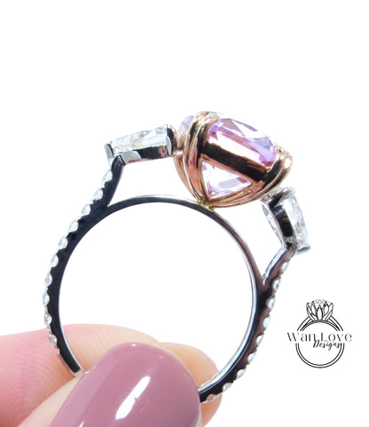 A close-up image of a person's hand holding a ring with a large pink gemstone, possibly a diamond, on top of it.
