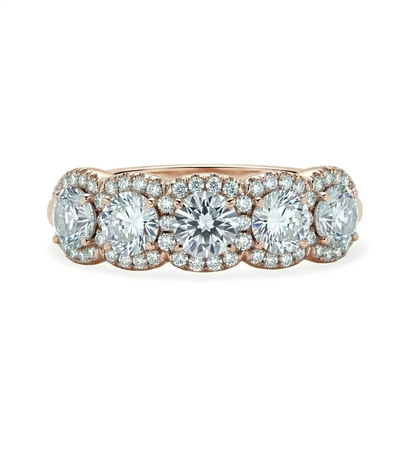 A rose gold ring with a row of five large, clear diamonds set in the center.