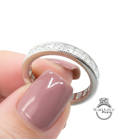 A close-up of a person's hand holding a silver ring with a row of diamonds on the band.