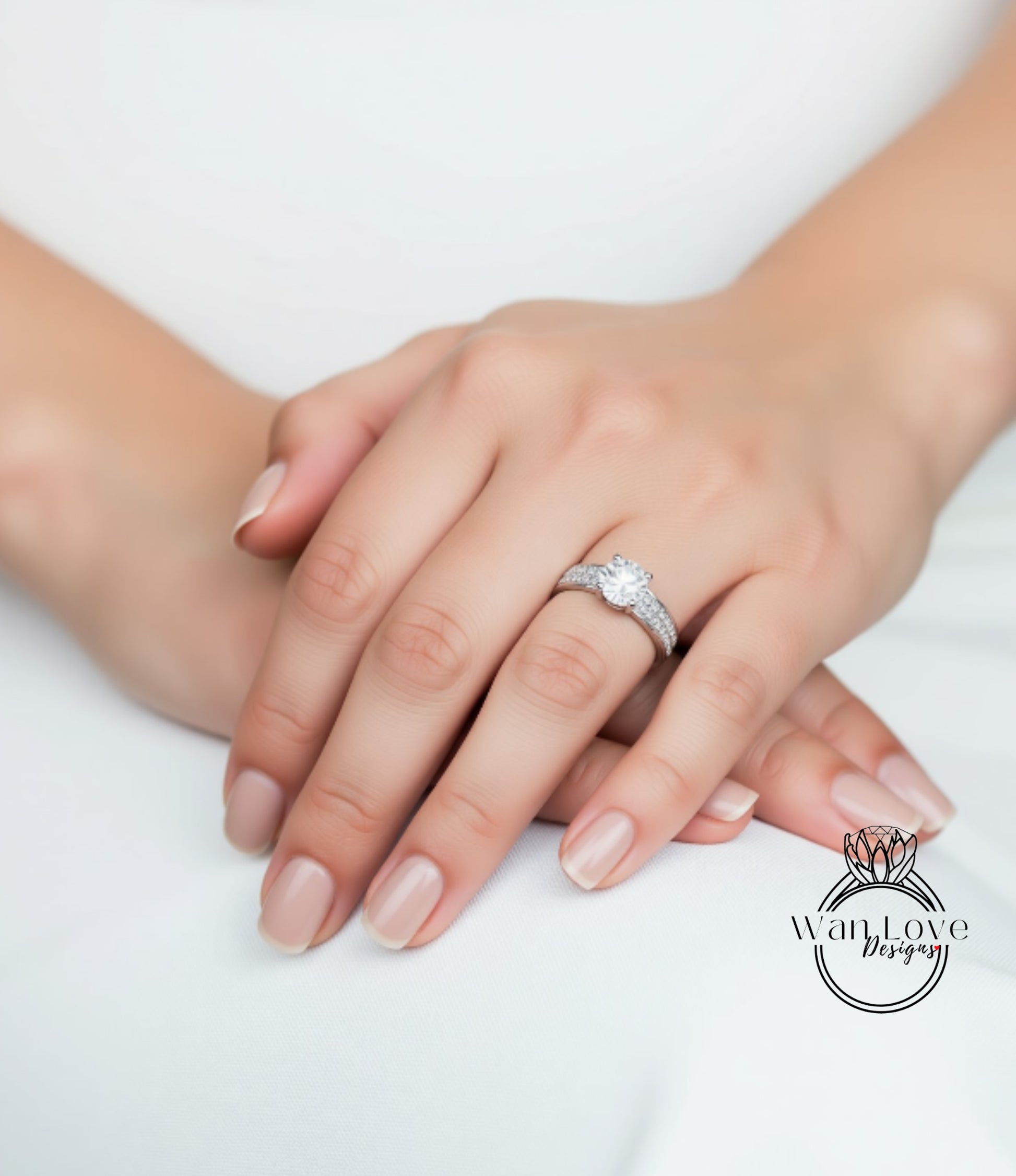 A close-up image of a hand wearing a diamond engagement ring, resting on a white surface.