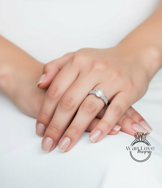 A close-up image of a hand wearing a diamond engagement ring, resting on a white surface.