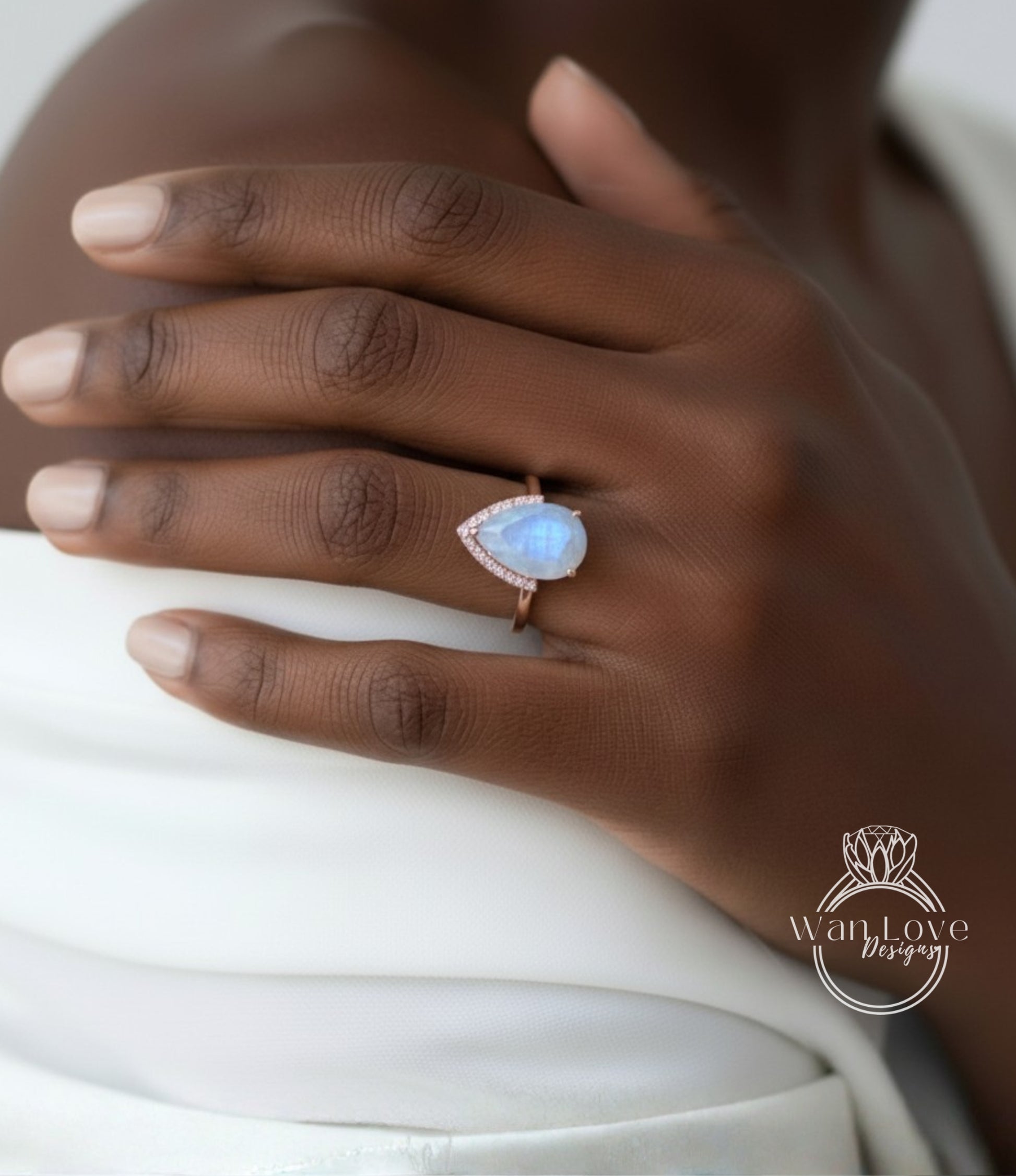 A close-up of a person's hand wearing a ring with a blue gemstone, resting on a white fabric.