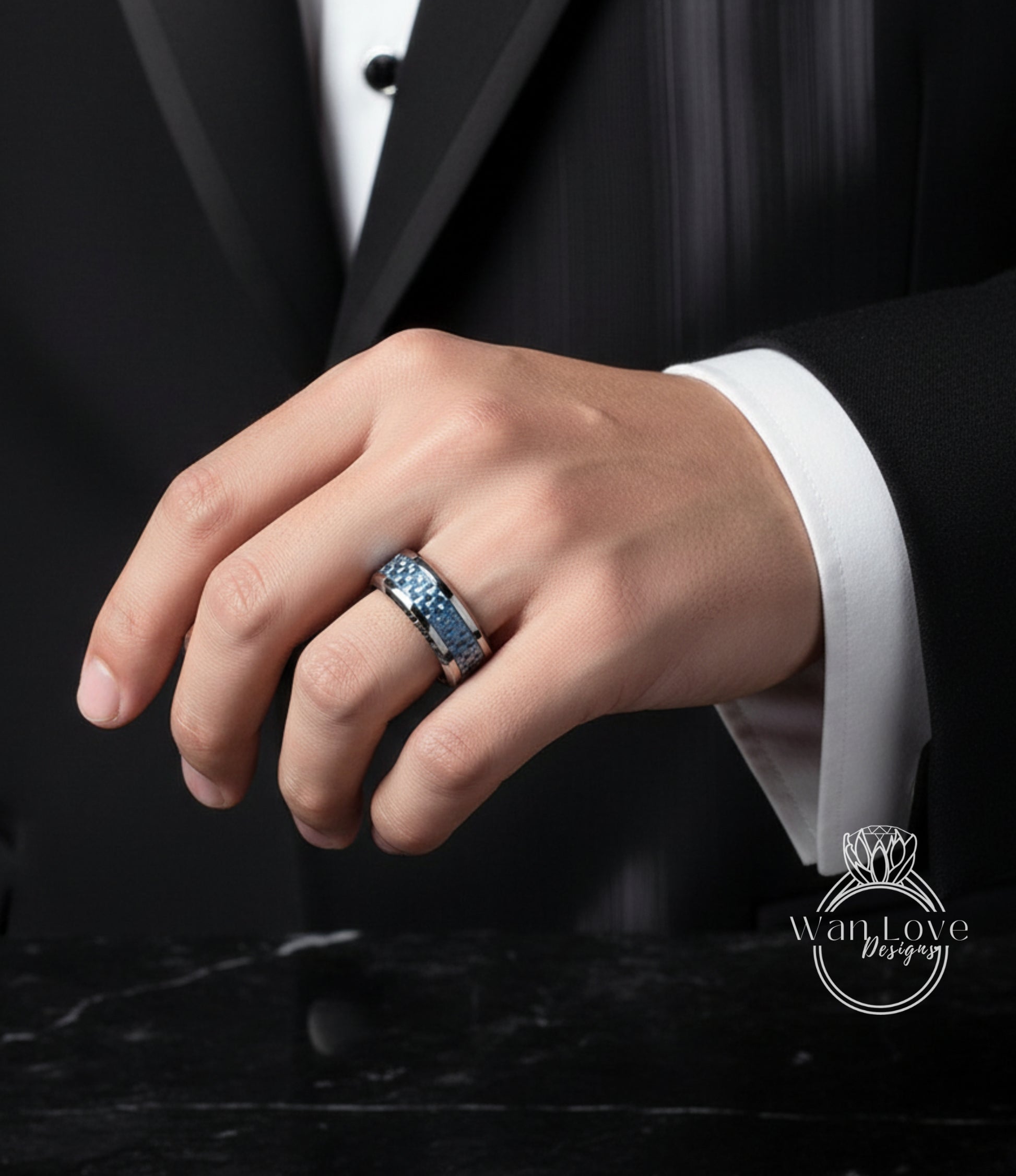 A close-up of a person's hand wearing a ring on the ring finger, with a black suit jacket visible in the background.