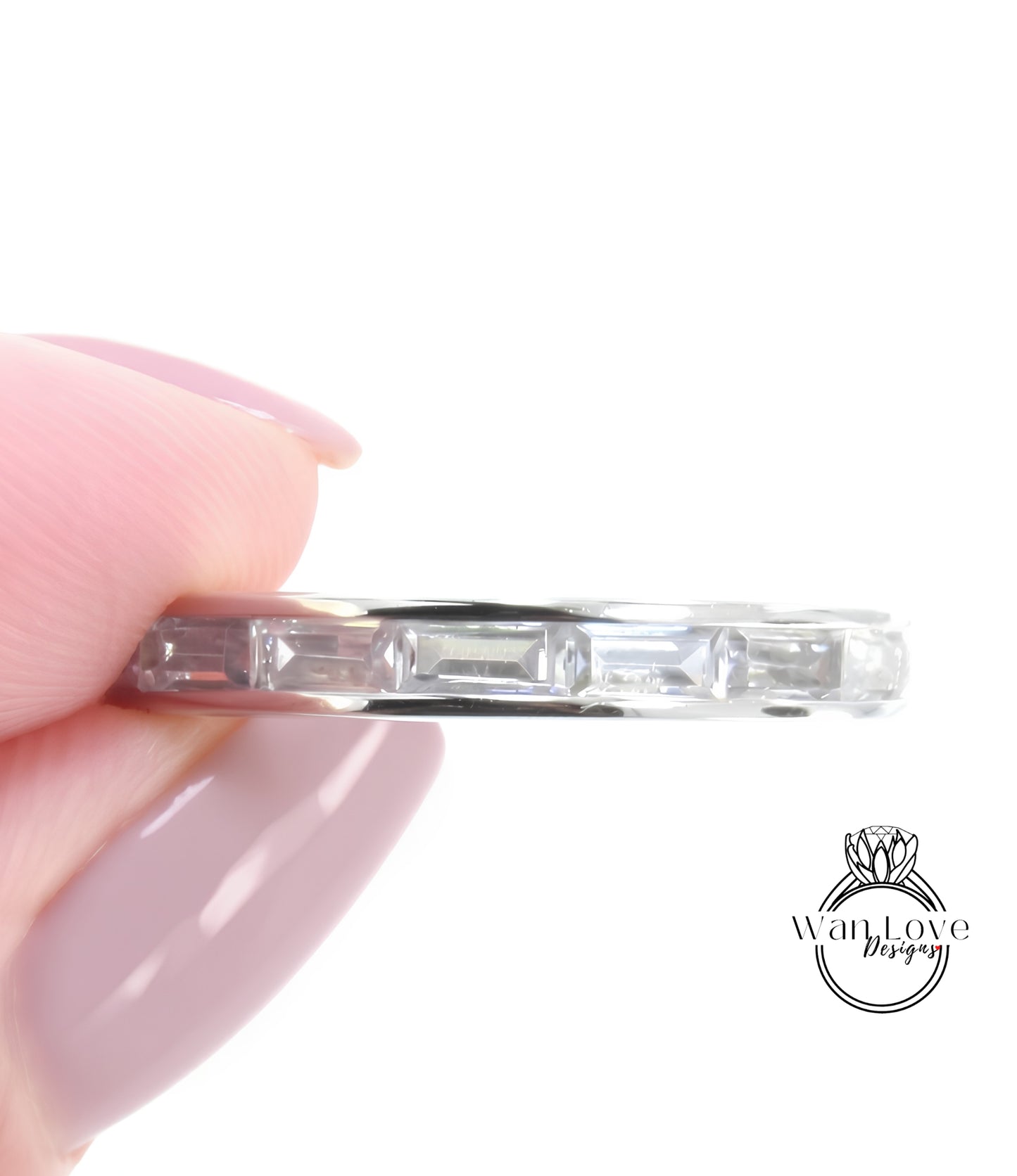 A close-up image of a person's hand holding a silver ring with a row of clear gemstones.