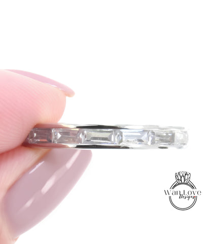 A close-up image of a person's hand holding a silver ring with a row of clear gemstones.