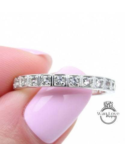 A close-up image of a person's hand holding a silver ring with a row of small diamonds set in it.