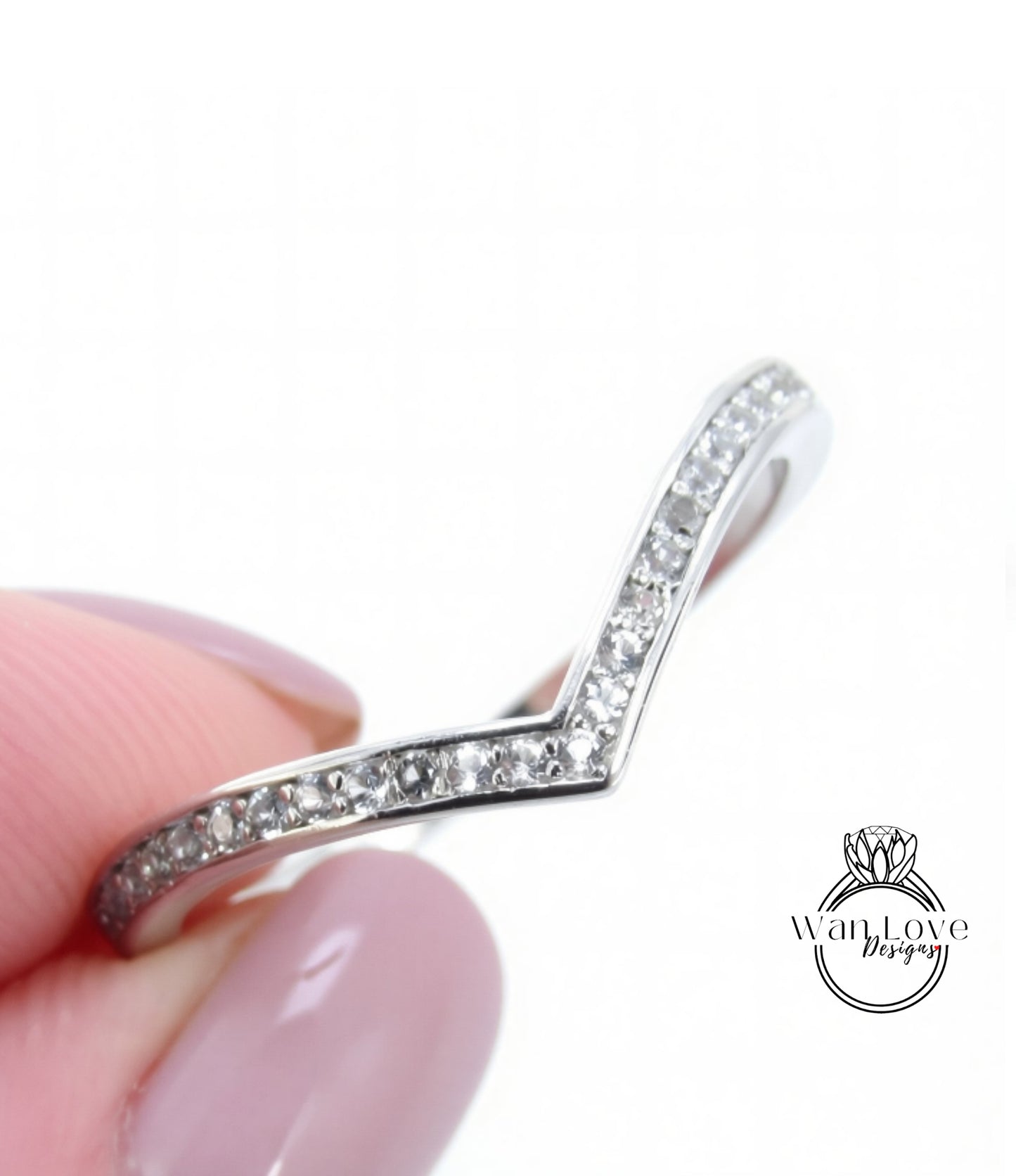 A close-up image of a person's hand holding a silver ring with a v-shaped design and small diamonds along the band.