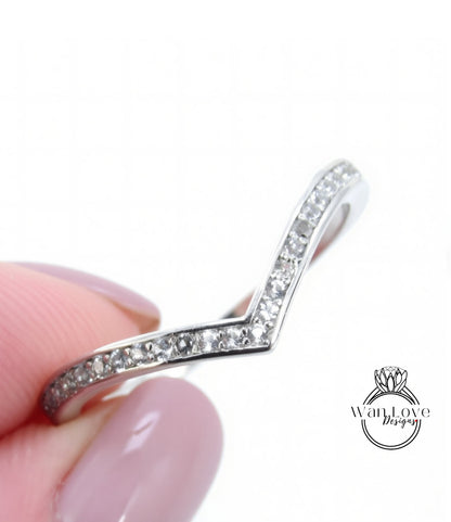 A close-up image of a person's hand holding a silver ring with a v-shaped design and small diamonds along the band.