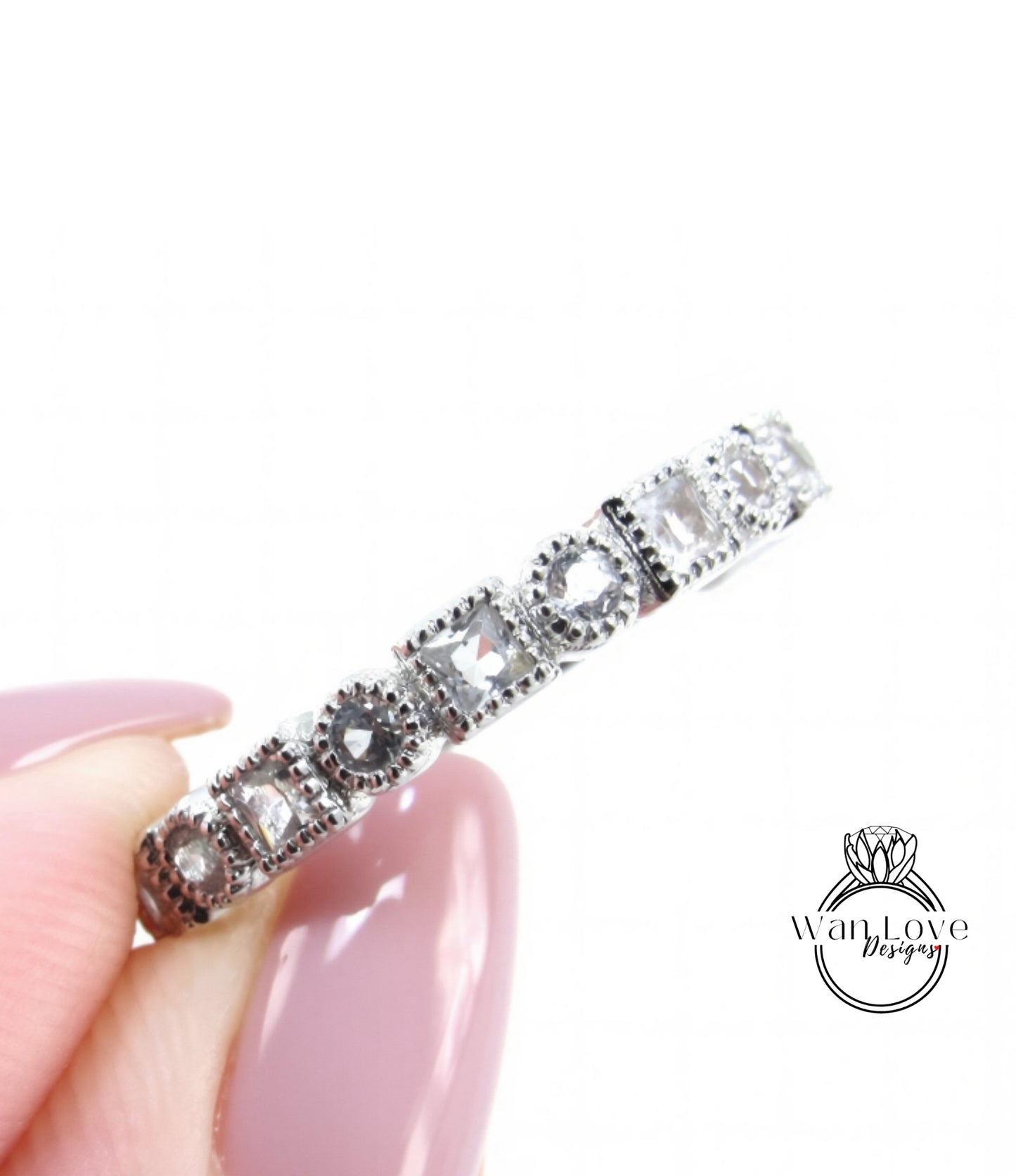 A close-up image of a person's hand holding a silver ring with a row of small diamonds on it.