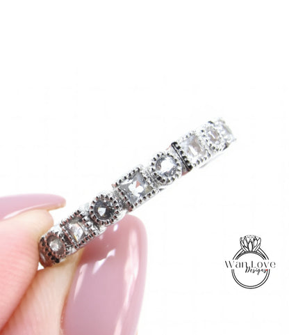 A close-up image of a person's hand holding a silver ring with a row of small diamonds on it.