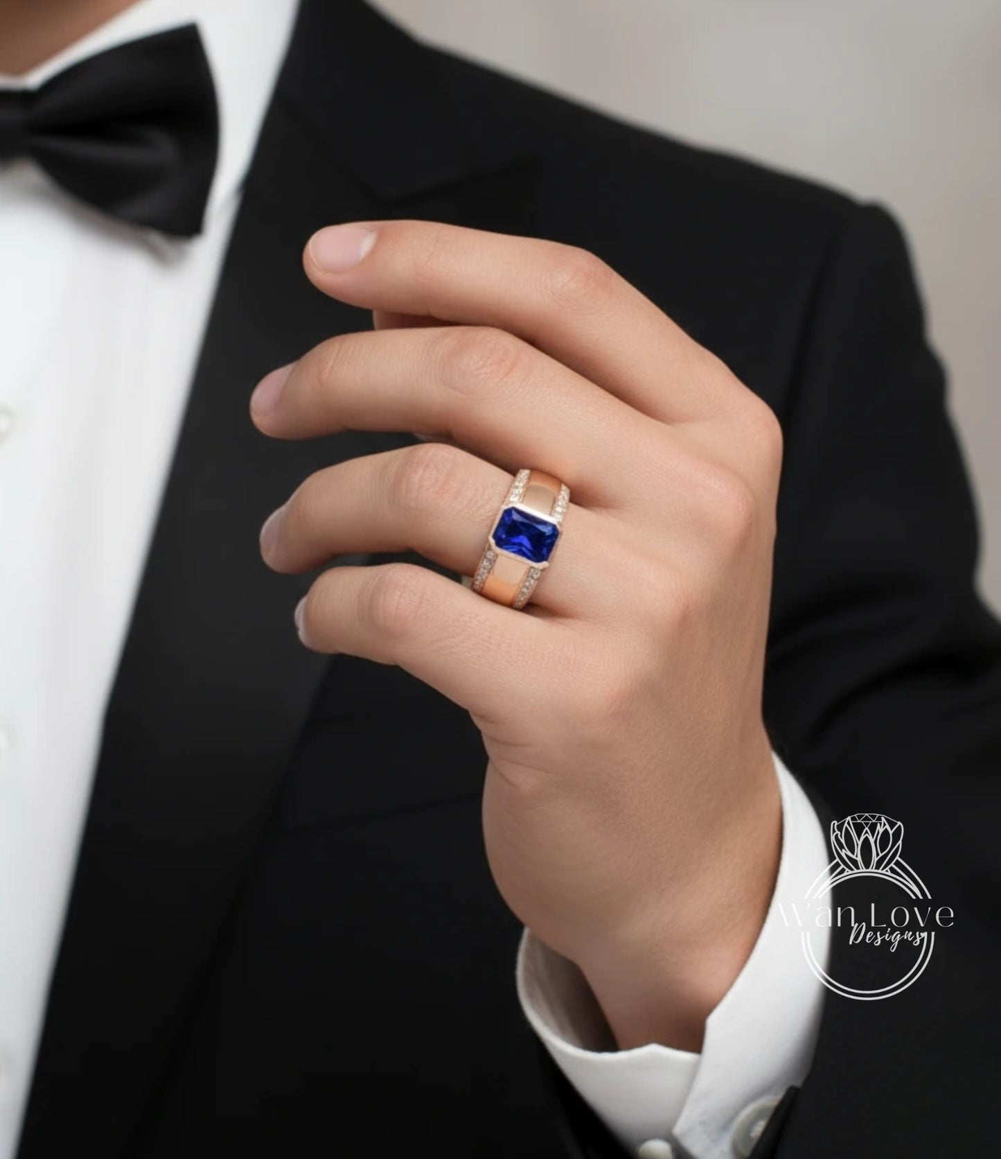 A close-up of a person's hand wearing a gold ring with a blue gemstone, wearing a black tuxedo.