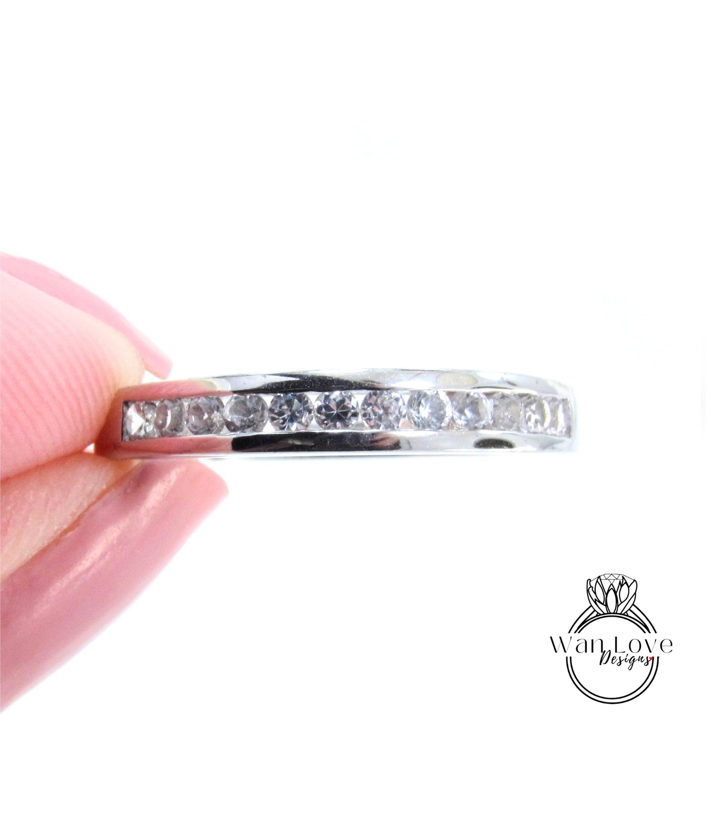 A close-up image of a person's hand holding a silver ring with a row of clear gemstones.