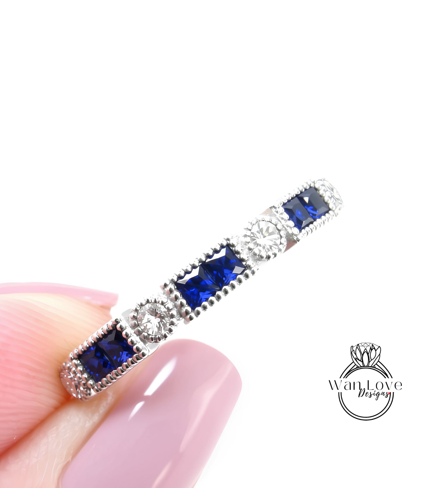 A close-up image of a person's hand holding a silver ring with blue gemstones.