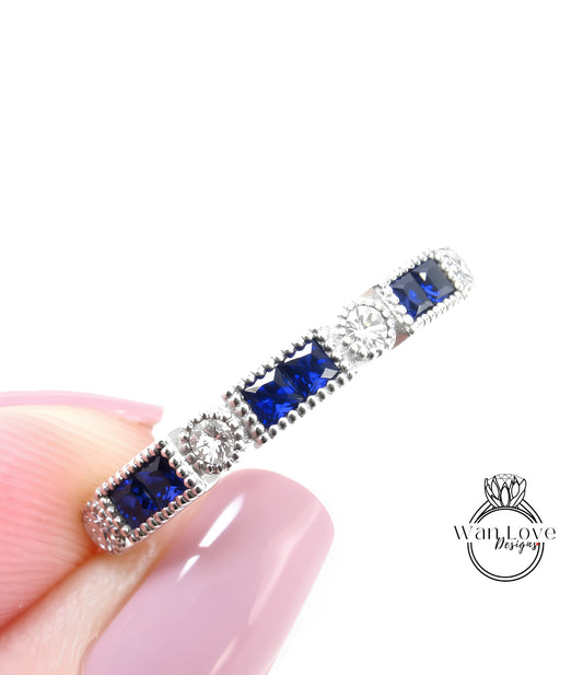A close-up image of a person's hand holding a silver ring with blue gemstones.