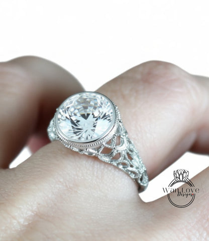 A close-up of a person's hand wearing a diamond engagement ring with a large central diamond surrounded by smaller diamonds and a decorative metal band.