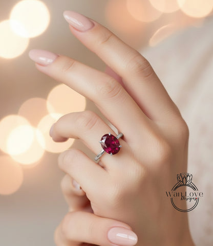 A close-up of a hand wearing a ring with a large, deep red gemstone.