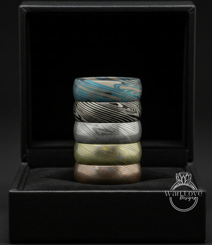 A stack of colorful rings is displayed in a black jewelry box against a dark background.